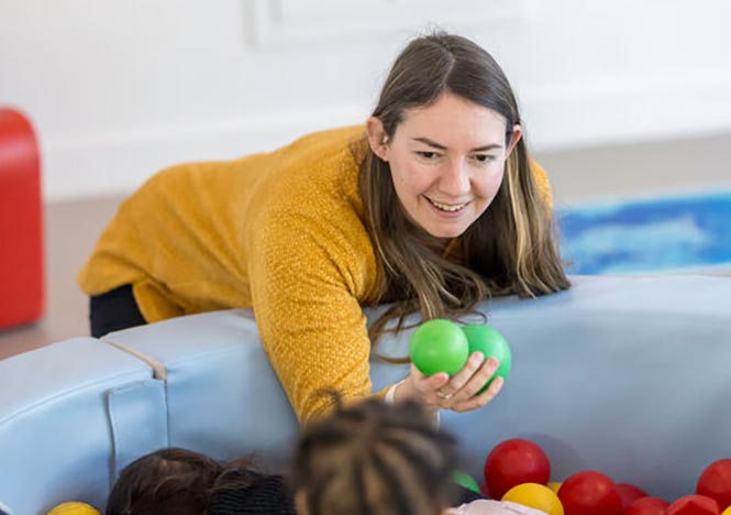 une éducatrice de jeunes enfants joue à un jeu de balles avec des enfants.
