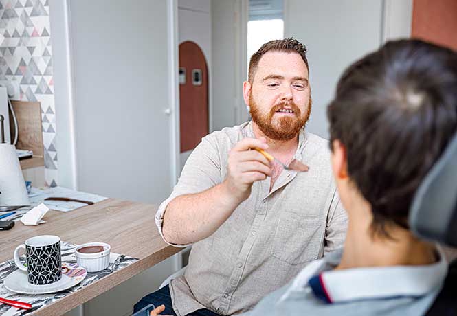Un accompagnant éducatif et social donne à manger à une personne en fauteuil tient la main d&#039;une personne âgée