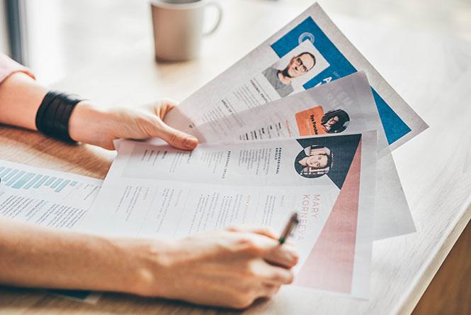 Comment trouver son premier emploi ? Une femme tenant trois CV dans sa main.